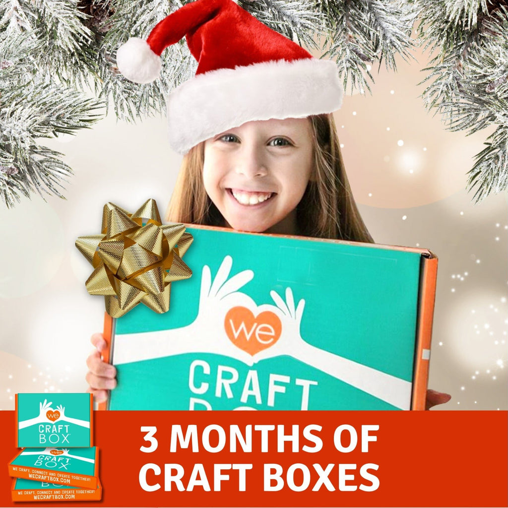 A child holding a craft box with a Santa hat on, presenting a gift-like craft box with '3 Months of Craft Boxes' label, indicating a craft subscription service.